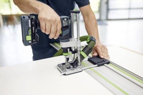 Eine Person, die ein Elektrowerkzeug auf einer weißen Oberfläche verwendet, wobei eine Hand das Werkzeug bedient und die andere eine Führungsschiene stabilisiert.