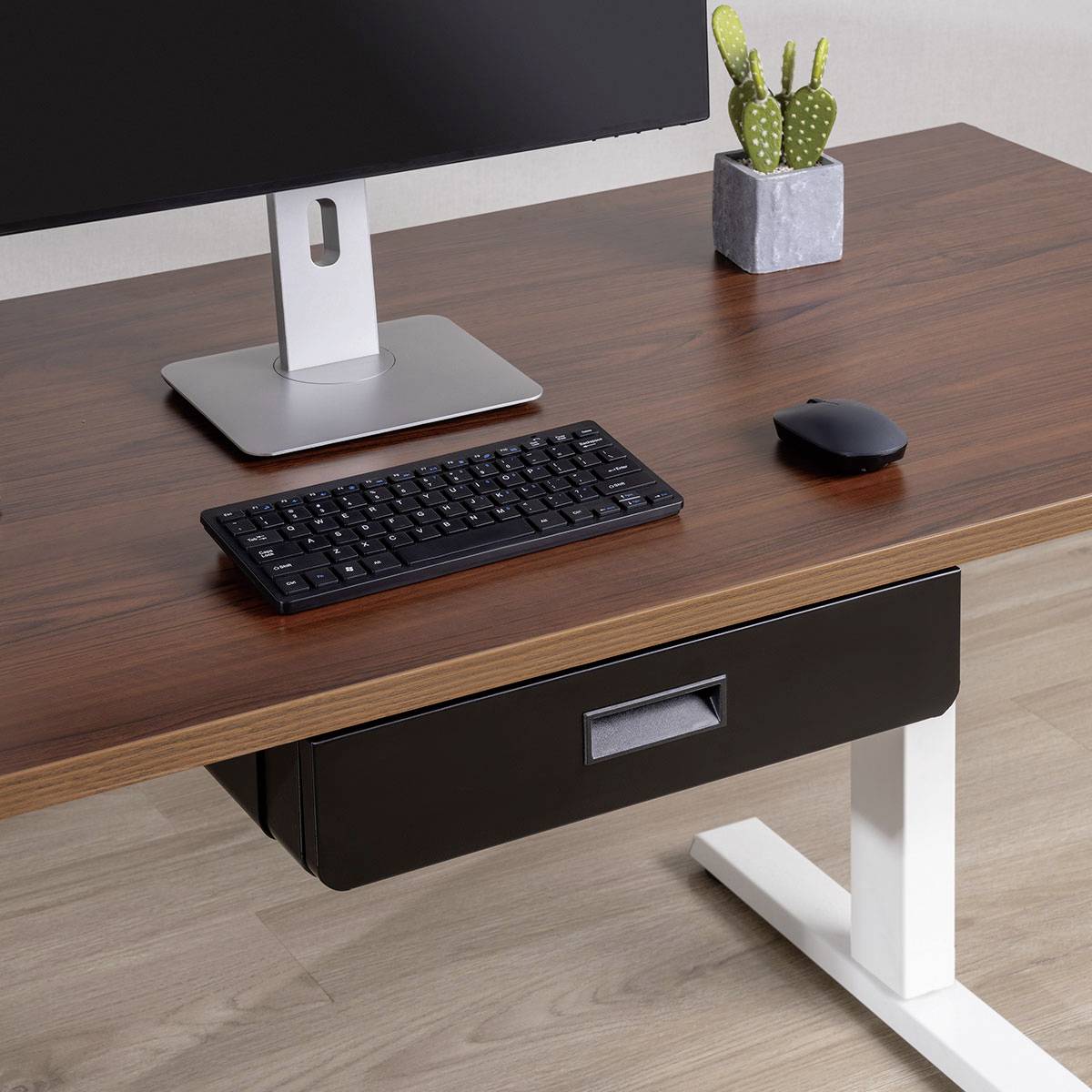 Ein Holzschreibtisch mit einem Monitor, einer Tastatur und einer Maus. Ein kleiner Topfkaktus steht neben dem Monitor. Der Schreibtisch hat ein weißes Metallbein.