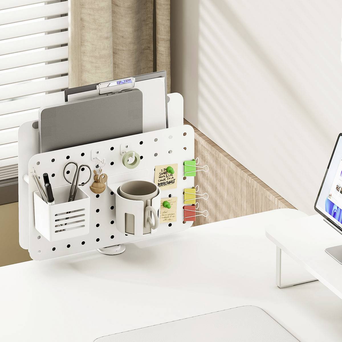 Ein weißer Schreibtischorganizer, der an einer Trennwand befestigt ist, hält Büromaterialien, einen Notizblock und Pflanzen, neben einem Laptop auf einem weißen Schreibtisch.