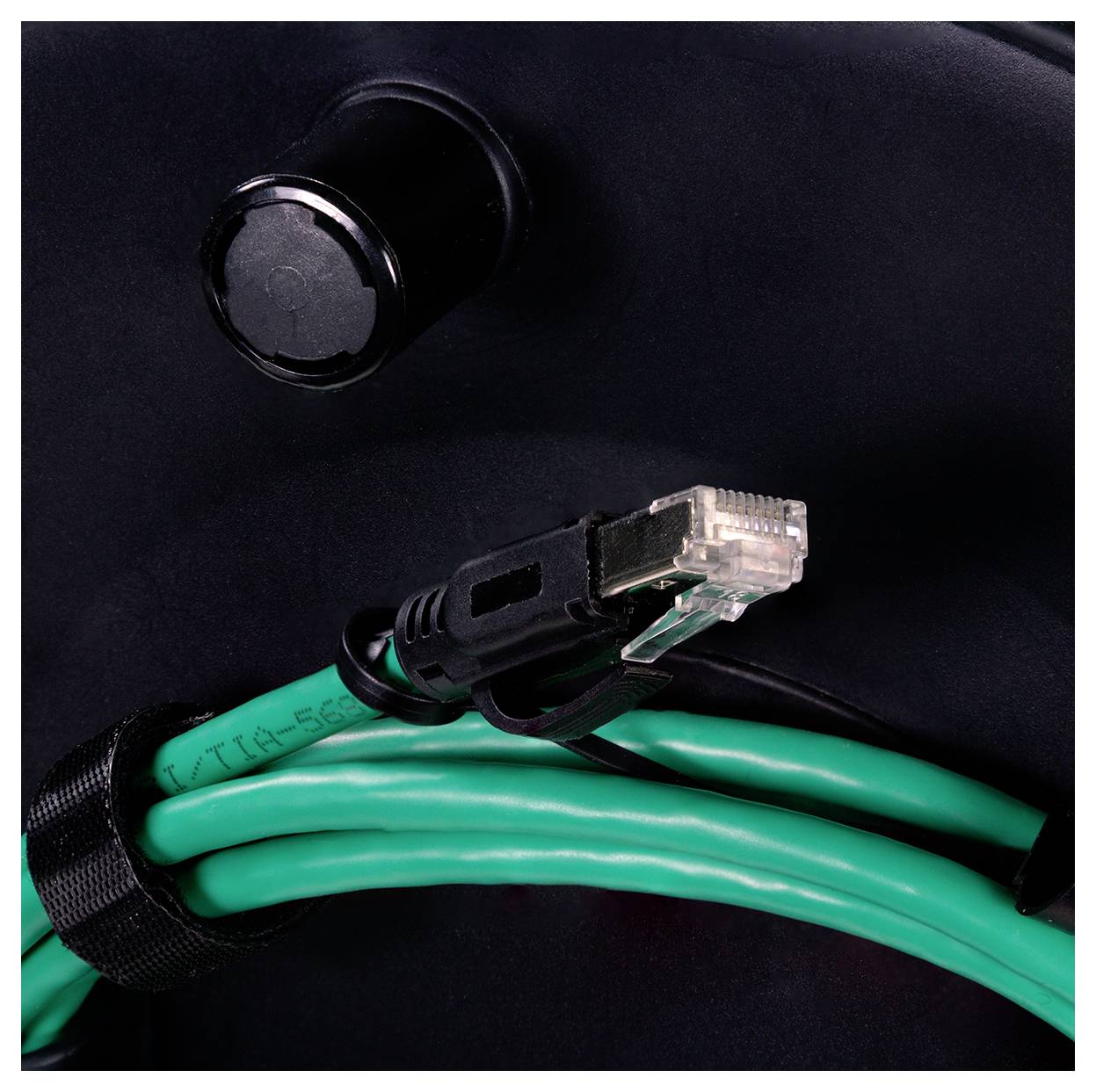 Ein Netzwerkkabel mit einem transparenten Stecker ist aufgewickelt und mit einem schwarzen Klettverschluss gesichert, und liegt vor einem schwarzen Hintergrund.