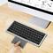 Eine Hand, die mit einem digitalen Touchpad neben einer drahtlosen Tastatur auf einem Holzschreibtisch interagiert; ein Computermonitor befindet sich im Hintergrund.