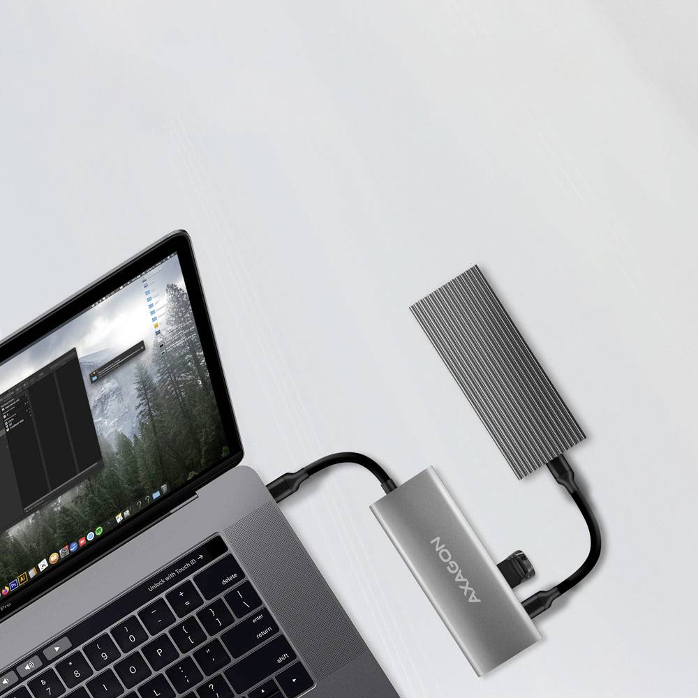 Ein Laptop mit einer Programmieroberfläche auf dem Bildschirm ist mit einer externen Festplatte verbunden, die mit "AXAGON" beschriftet ist und auf einer weißen Oberfläche steht.