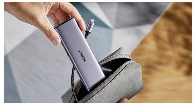 Eine Hand legt eine graue tragbare Powerbank mit angeschlossenem Kabel in ein kleines graues Reißverschlussetui vor einem geometrisch gemusterten Hintergrund.