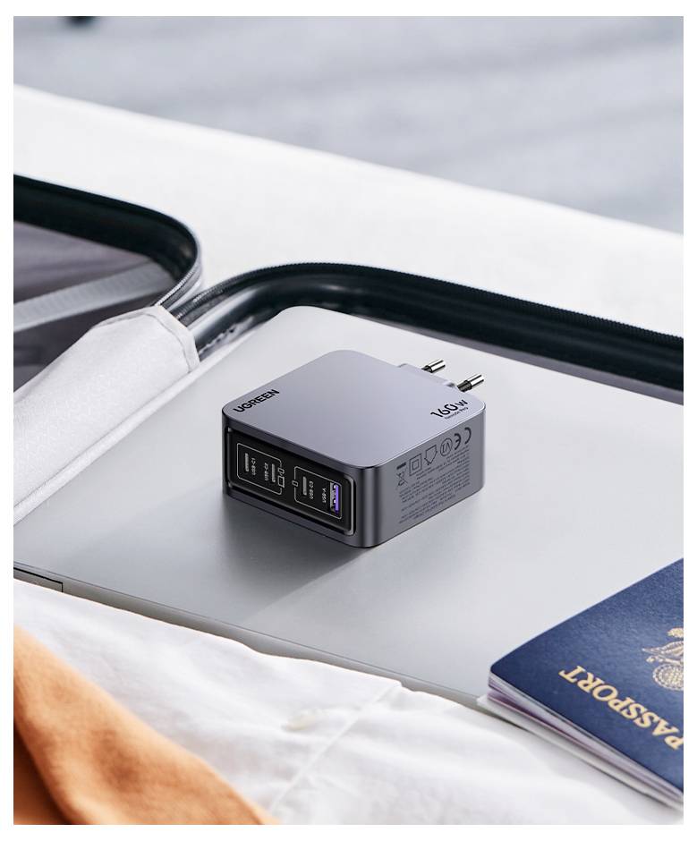 Ein Reiseadapter mit mehreren USB-Anschlüssen liegt auf einem geschlossenen Laptop neben einem Reisepass und deutet auf Reisevorbereitungen hin.
