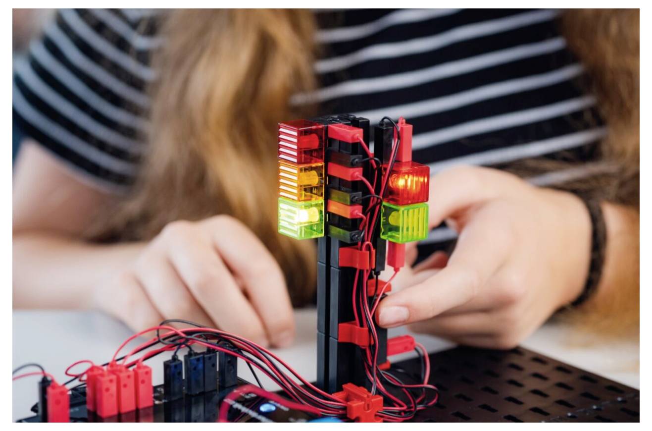 Eine Person baut ein kleines elektronisches Projekt mit einem Ampelmodell, das rote, gelbe und grüne Lichter auf einer Leiterplatte umfasst.