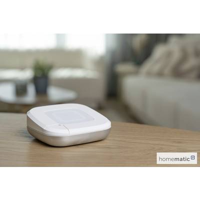 Ein Smart-Home-Gerät steht auf einem Holztisch in einem Wohnzimmer. Der Hintergrund zeigt verschwommene Sofas und eine Pflanze und schafft eine gemütliche Atmosphäre.
