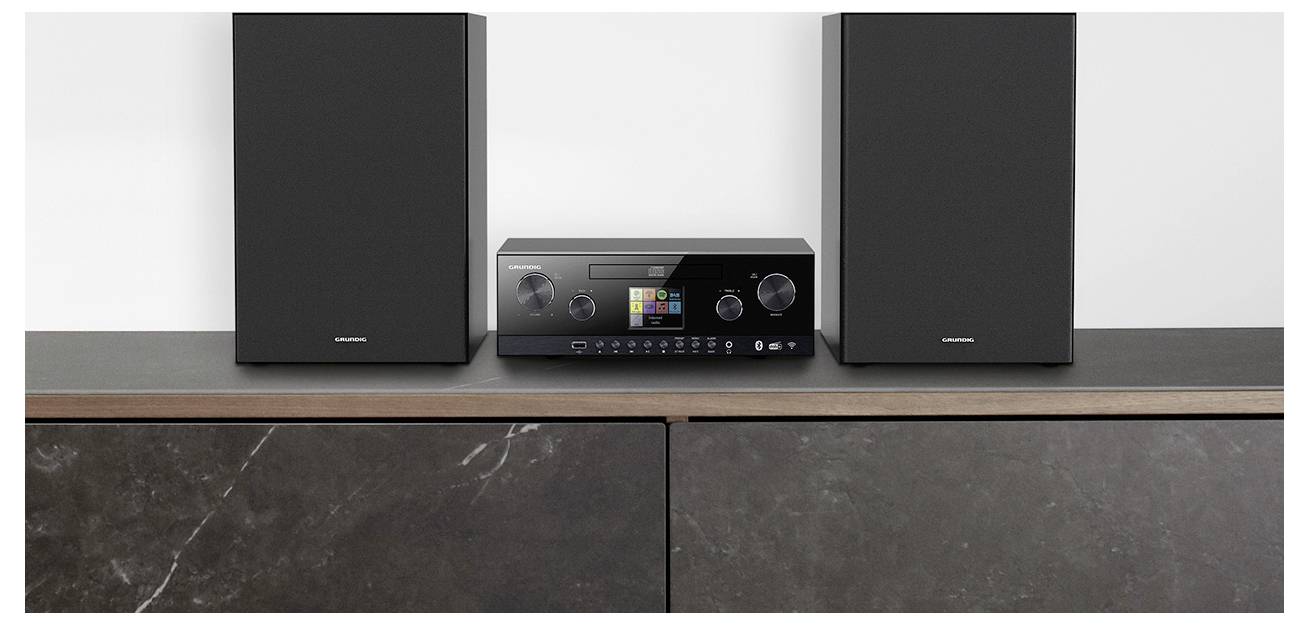 Ein schwarzes Stereosystem mit Lautsprechern steht auf einem dunklen Holzschrank und verfügt über ein digitales Display und verschiedene Bedienungsknöpfe.