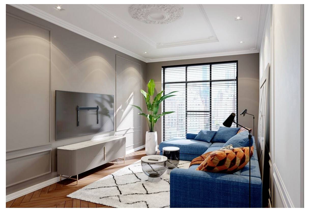 Ein moderner Wohnraum mit einem blauen Ecksofa, bunten Kissen, einer Pflanze, einem an der Wand montierten Fernseher und einem großen Fenster mit Jalousien.