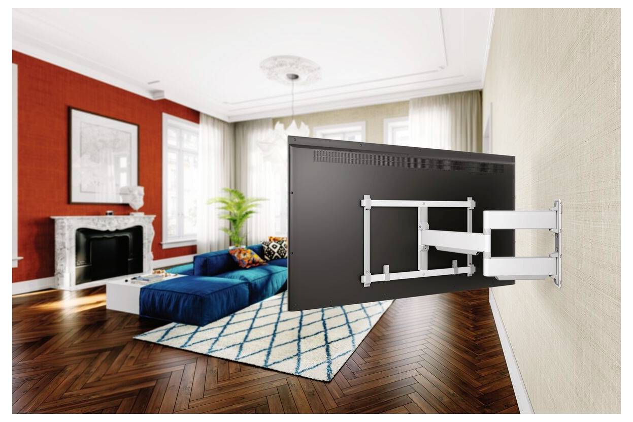 Eine wandmontierte TV-Halterung bringt einen Flachbildfernseher in ein modernes Wohnzimmer mit blauem Sofa und geometrischem Teppich und schafft dabei eine geräumige Raumaufteilung.