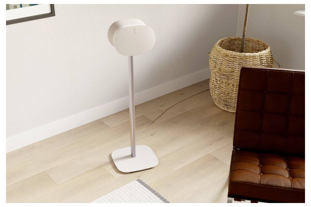 Ein hoher, moderner Standventilator mit minimalistischem Design steht auf einem Holzboden neben einem braunen Stuhl und einem geflochtenen Korb in einem Wohnzimmer.