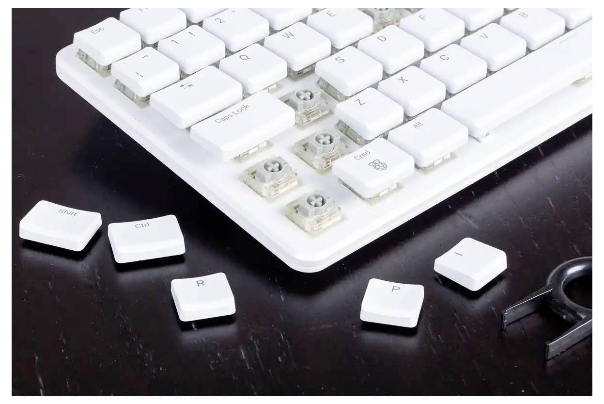 Eine weiße Tastatur auf einer dunklen Oberfläche mit mehreren entfernten Tasten, die die Schalter darunter offenlegen. Ein Keycap-Abzieher ist in der Nähe sichtbar.