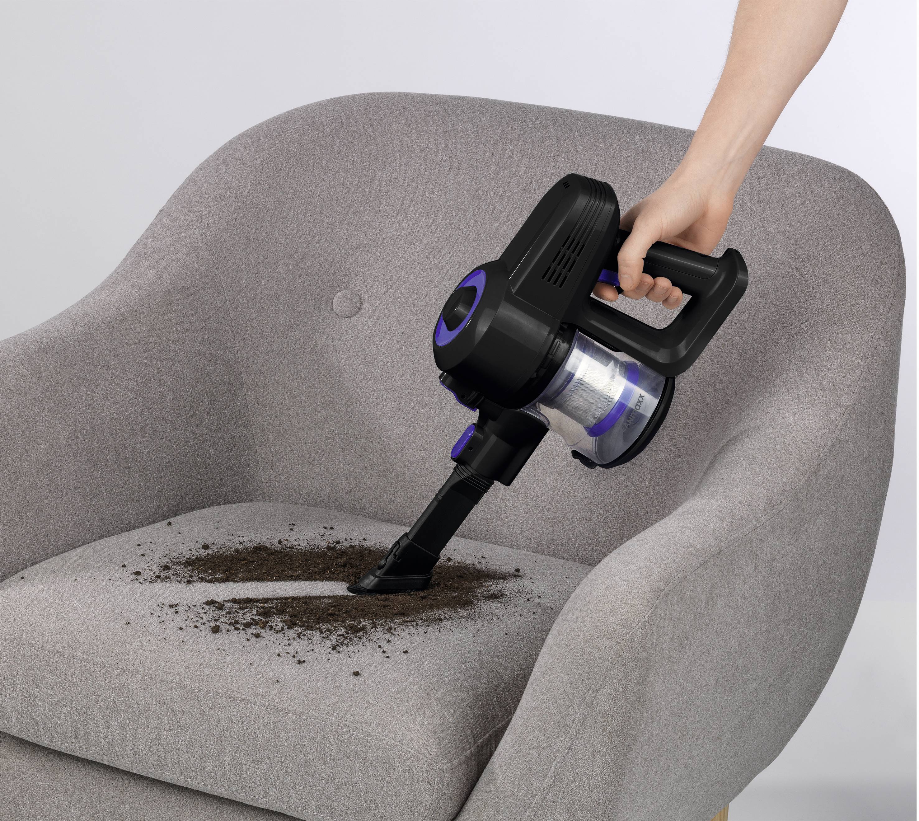 Eine Person benutzt einen tragbaren Staubsauger, um Schmutz von einem grauen Polsterstuhl zu entfernen und zeigt damit eine effektive Reinigungsmethode.