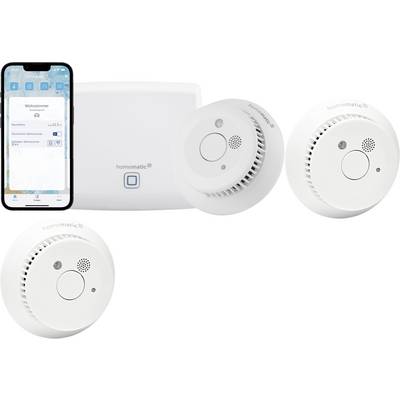 Ein Smartphone, das eine Smart-Home-App zeigt, neben einer Steuereinheit und drei runden, weißen Rauchmeldern.