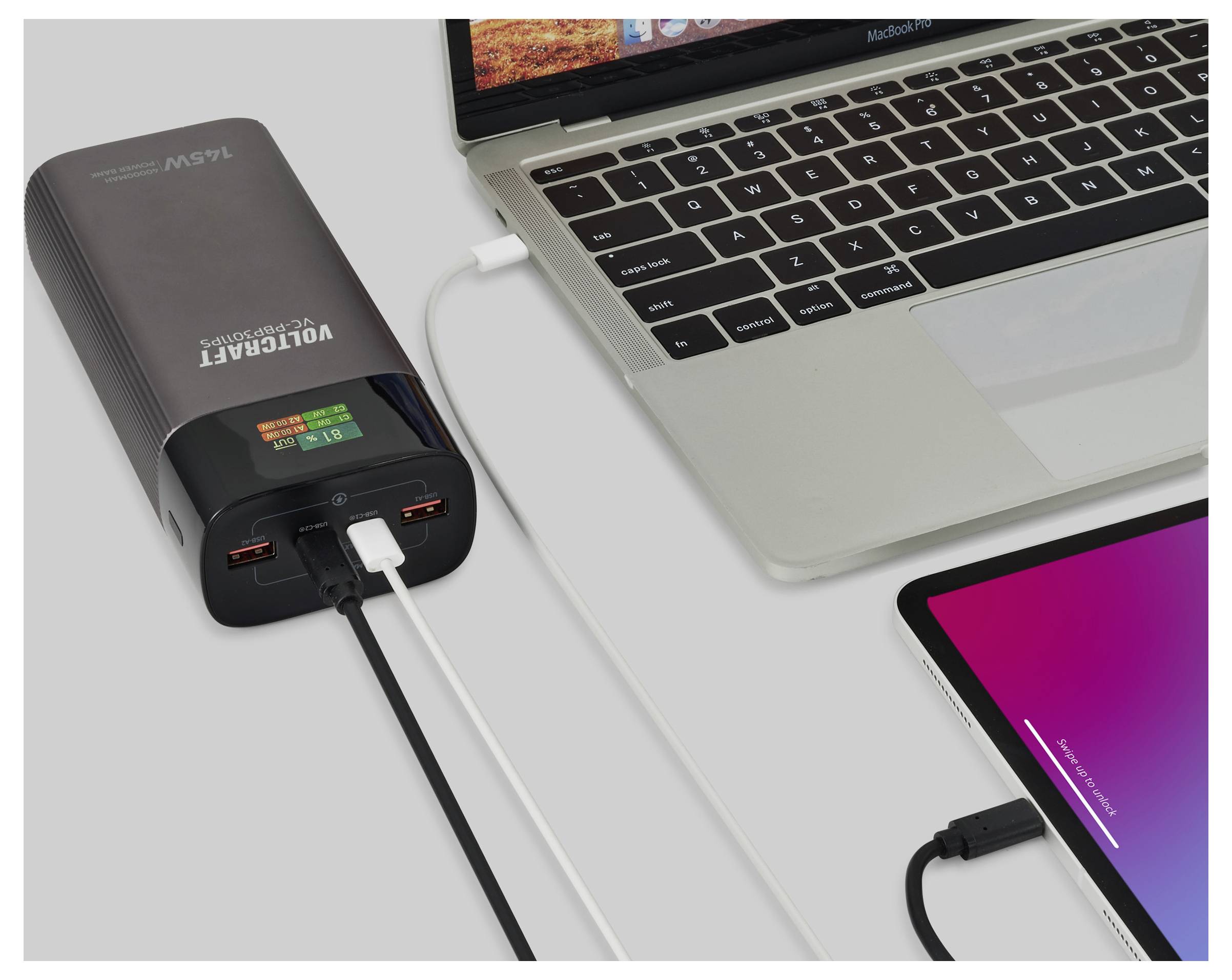 Ein Laptop und ein Tablet laden, verbunden mit einem Powerbank mit der Aufschrift "Volcraft 156Wh", was seine Rolle als mobile Ladelösung veranschaulicht.