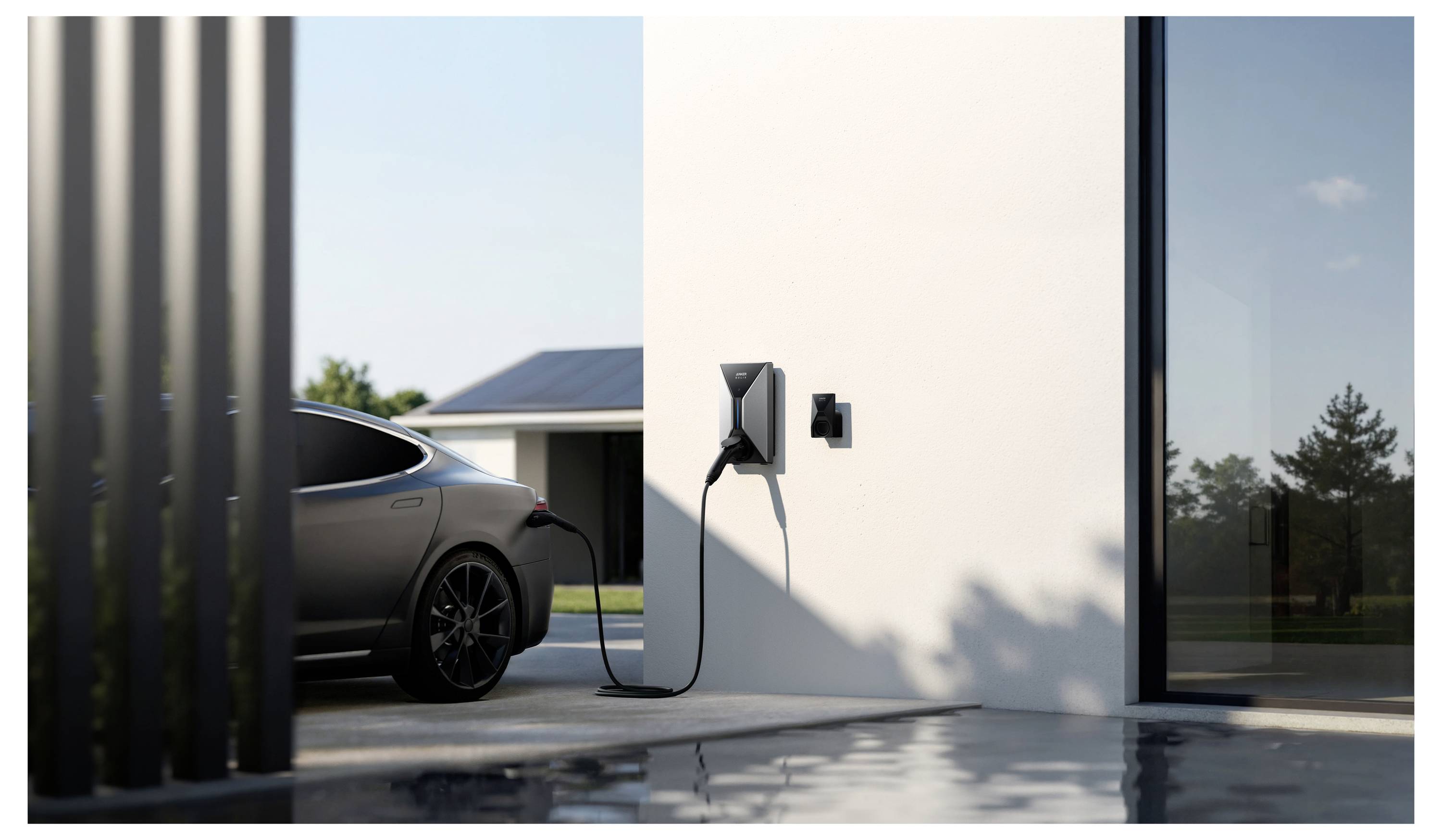 Ein schlankes schwarzes Auto steht geparkt und lädt über eine wandmontierte Ladestation an der Außenseite eines modernen Gebäudes, mit einem klaren Himmel und Bäumen im Hintergrund.