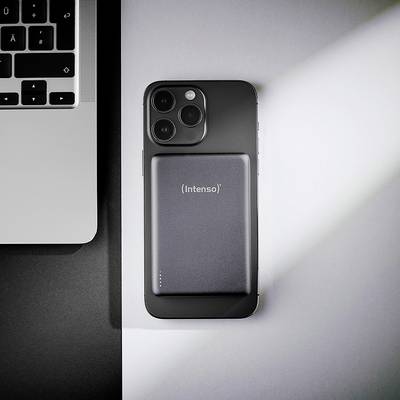Ein Smartphone auf einem Schreibtisch mit einer rechteckigen, tragbaren Powerbank, die an seiner Rückseite befestigt ist. Ein Teil einer Laptop-Tastatur ist links sichtbar.