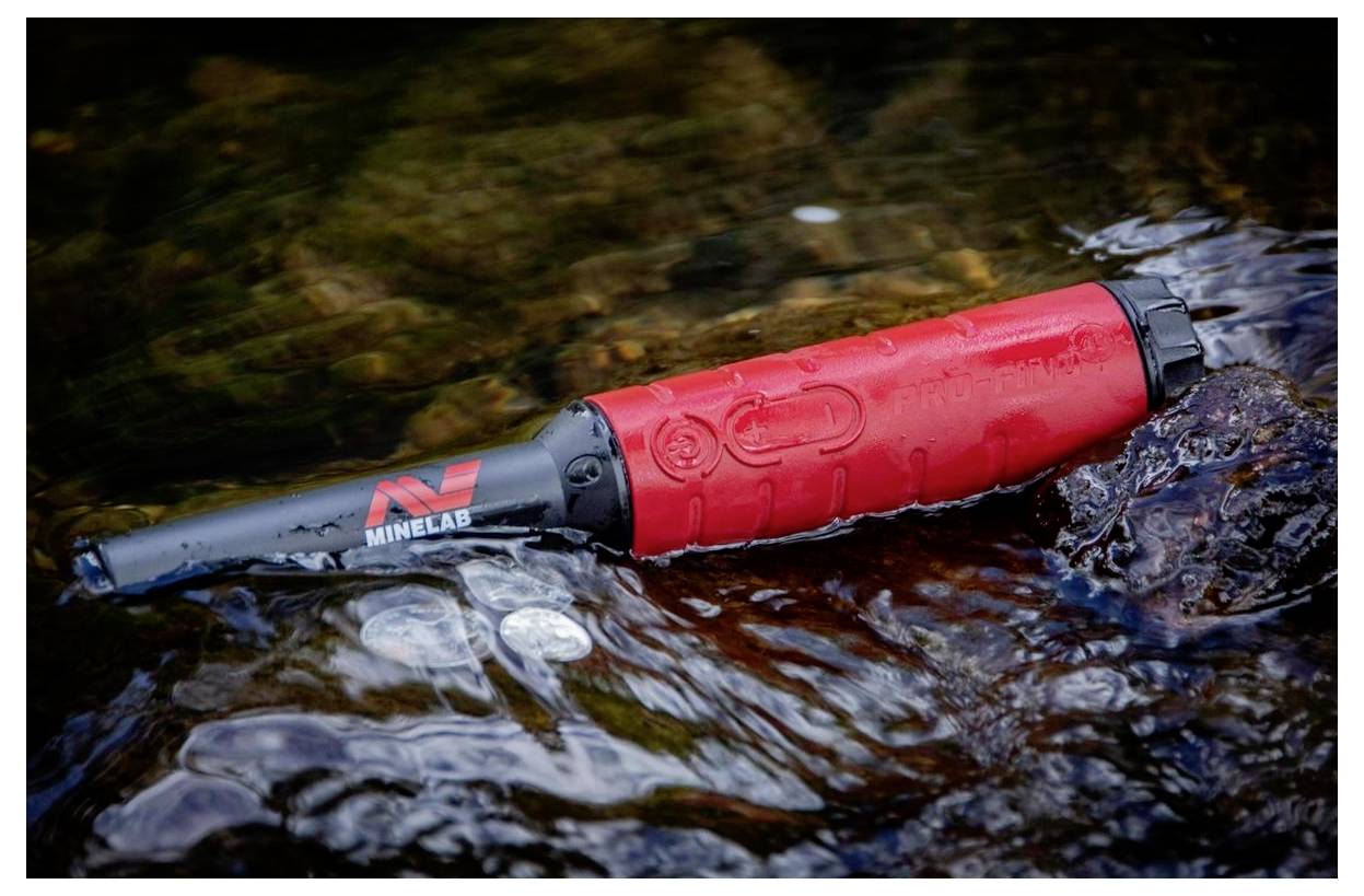 Ein roter und schwarzer tragbarer Metallsuchgerät liegt auf nassen Steinen in seichtem Wasser und zeigt damit seine Wasserdichtigkeit.