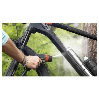 Eine Person verwendet einen Schlauchadapter, um Wasser zu spritzen und einen schwarzen Fahrradrahmen in der Nähe einer Waldlandschaft zu reinigen.