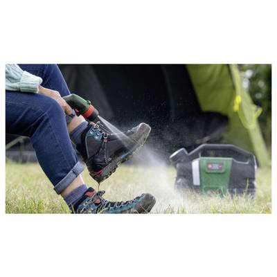 Eine Person, die schlammige Wanderstiefel mit einer tragbaren Wassersprühflasche reinigt, neben einem grünen Zelt auf Gras. Eine mobile Stromversorgungseinheit befindet sich in der Nähe.