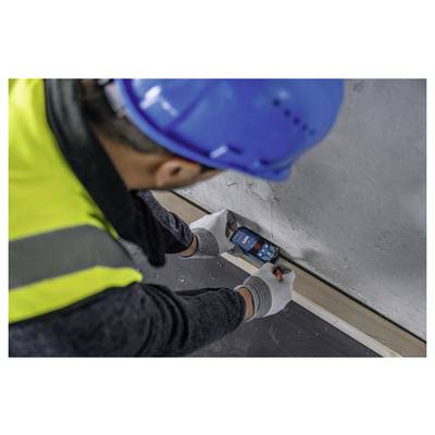 Ein Bauarbeiter mit blauem Helm und Sicherheitsweste misst mit einem Laserdistanzmessgerät eine Wand und konzentriert sich dabei auf präzise Messungen.