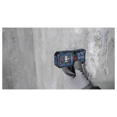 Eine Person mit einem Handschuh verwendet einen digitalen Entfernungsmesser an einer Betonwand. Das Gerät zeigt '1,902' an.