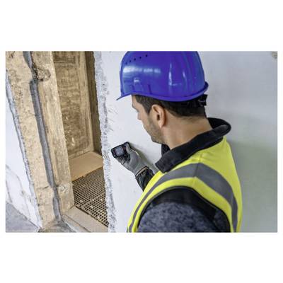 Ein Bauarbeiter mit blauem Schutzhelm und gelber Warnweste nutzt ein tragbares Gerät, um die Dicke einer Betonwand auf einer Baustelle zu messen.