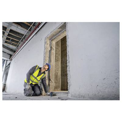 Ein Bauarbeiter in einer gelben Warnweste und einem blauen Schutzhelm untersucht einen Türrahmen in einem unfertig Gebäude und prüft dessen Ausrichtung und Stabilität.