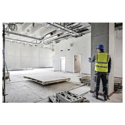 Bauarbeiter im Warnwesten und Schutzhelm bewertet einen leeren Betonraum im Innenbereich und deutet damit auf laufende Renovierungsarbeiten hin.