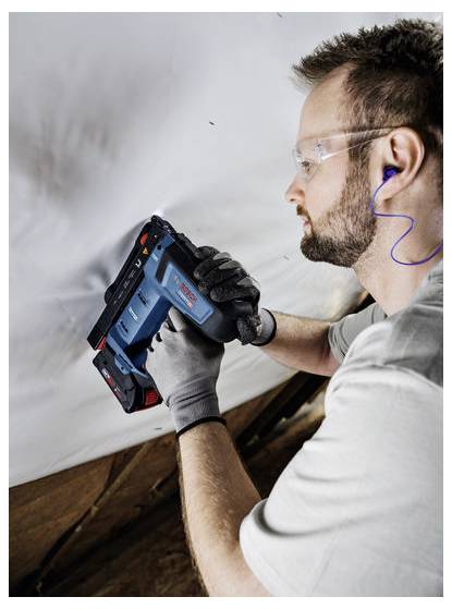 Arbeiter mit Sicherheitsausrüstung verwendet ein kabelloses Werkzeug, um Material über Kopf zu befestigen und damit eine Heimwerkeraufgabe zu demonstrieren.