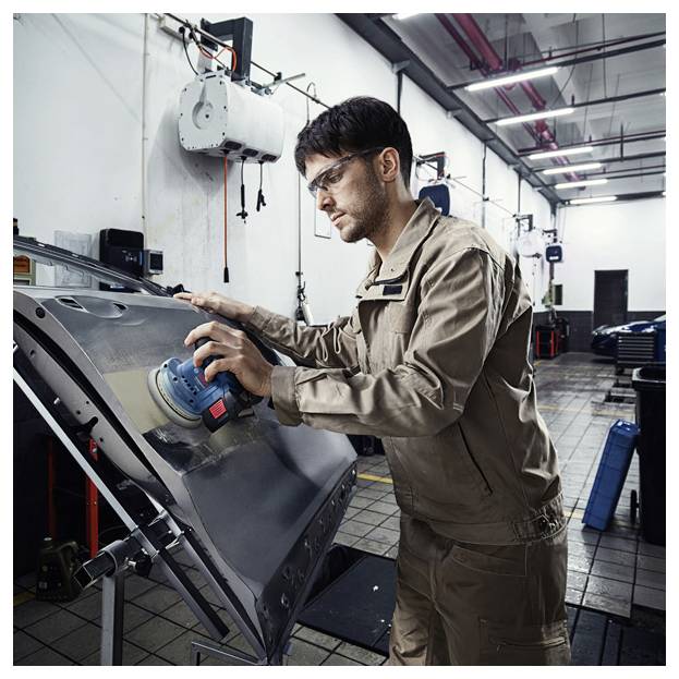 Ein Mann in einer Werkstatt, der eine Autotür mit einem elektrischen Schleifgerät poliert und einen beigen Arbeitsanzug und Sicherheitsbrille trägt. Die Werkstatt ist gut beleuchtet.