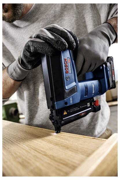 Eine Person mit Handschuhen verwendet einen Bosch-Nagler, um Holzstücke zu befestigen, mit Fokus auf sorgfältige Ausrichtung und Präzision in einer Werkstattumgebung.