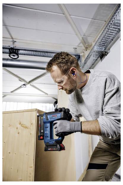 Eine Person in Sicherheitsausrüstung, die ein Elektrowerkzeug verwendet, um an einem Holzschrank in einer Werkstattumgebung zu arbeiten.