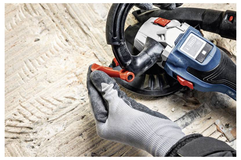 EineHand mit Handschuh bedient ein blaues und schwarzes Elektrowerkzeug auf einer strukturierten Oberfläche und konzentriert sich dabei darauf, einen roten Hebel an dem Gerät einzustellen.