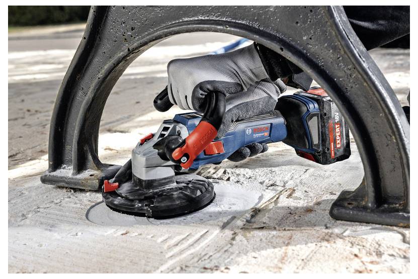 Eine Person verwendet eine Bosch Professional Akku-Winkelschleifer, um einen Betonboden zu glätten und konzentriert sich dabei auf einen Abschnitt zwischen Metallrahmenbeine.