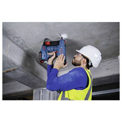 Eine Person in einer Sicherheitsweste und einem Helm bohrt mit einem Elektrowerkzeug in eine Betondecke und arbeitet an einer Baustelle oder Renovierung.