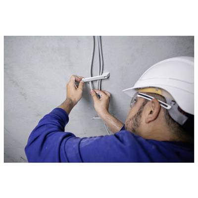 Eine Person mit Schutzhelm und Sicherheitsbrille installiert elektrische Leitungsrohre an einer Wand und verwendet ein Werkzeug, um Metallhalterungen zu befestigen.