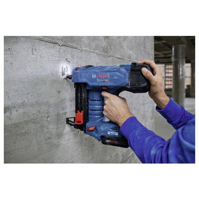 Eine Person verwendet einen blauen Bosch-Betonnagler, um Material in eine Betonwand in einer Bauumgebung zu befestigen.
