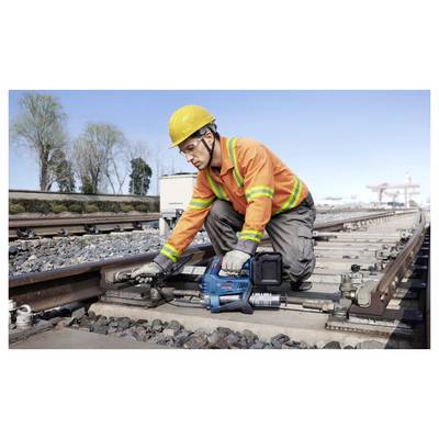 Ein Arbeiter in Sicherheitsausrüstung bedient eine Maschine auf Eisenbahnschienen unter einem klaren Himmel und konzentriert sich auf Wartungs- oder Reparaturaufgaben.