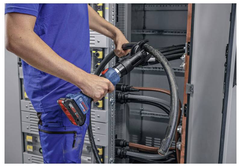 Eine Person in blauer Arbeitskleidung benutzt ein Elektrowerkzeug, um große Kabel in einem offenen Elektroschrank zu verbinden, möglicherweise während einer Installation oder Wartung.