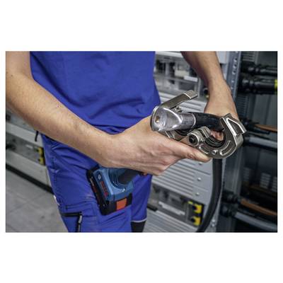 „Person in blauer Uniform, die ein Crimpwerkzeug in der Nähe von Elektrotafeln hält und sich darauf vorbereitet, Leitungen zu verbinden oder anzupassen."