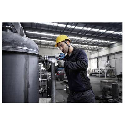 Ein Arbeiter in Sicherheitsausrüstung bedient ein Elektrowerkzeug an industriellen Rohrleitungen im Inneren einer großen Fabrik und unterstreicht dabei den Fokus auf industrielle Wartung.