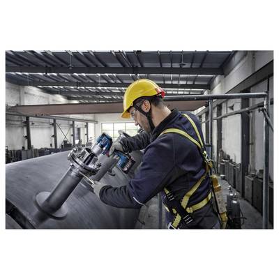 Ein Arbeiter in einem Sicherheitsgeschirr und Helm benutzt ein Elektrowerkzeug an einer großen Metallstruktur in einer Fabrikhalle.