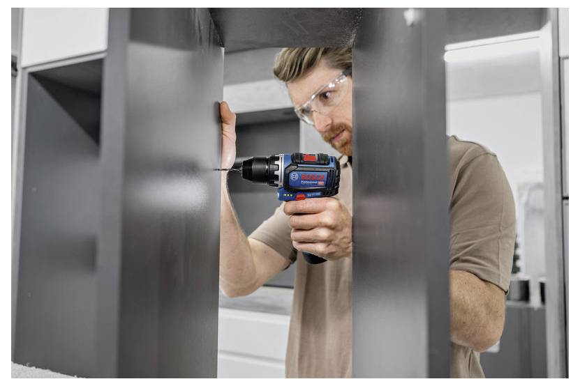 Eine Person mit Sicherheitsbrille verwendet eine Bohrmaschine, um ein Loch in einer Metalloberfläche in einer Werkstattumgebung zu bohren.