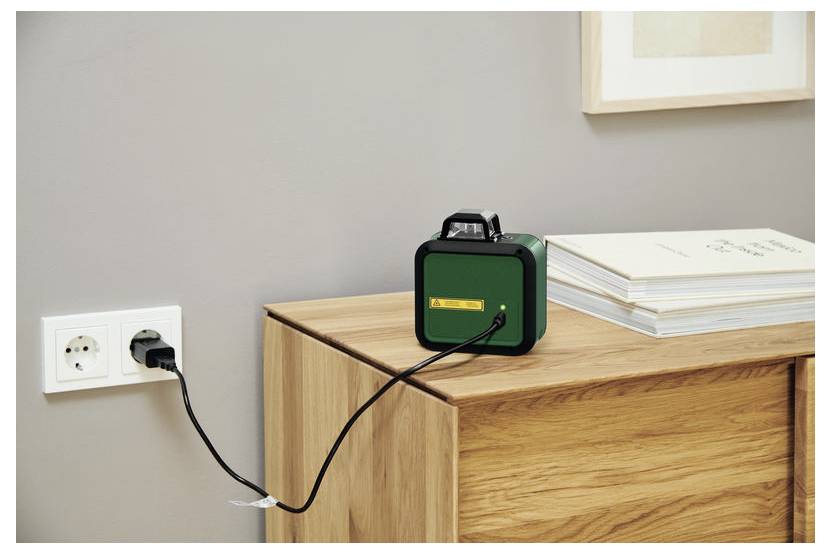 Ein tragbares grünes Radio, das in eine Wandsteckdose an einem Holzschrank neben gestapelten Büchern angeschlossen ist und darauf hindeutet, dass es gerade aufgeladen wird.