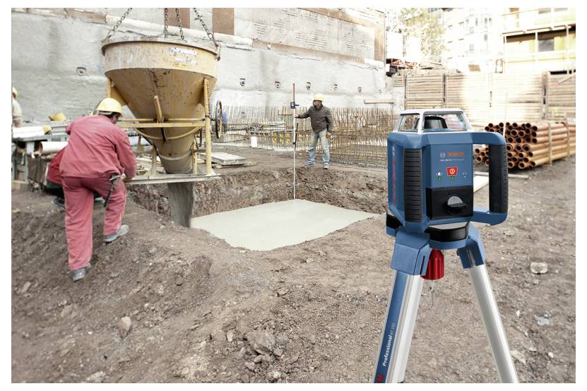 Baustelle mit Arbeitern, die Beton in ein Fundament gießen. Ein Laserebenen-Stativ ist im Vordergrund zu sehen, um eine präzise Nivellierung sicherzustellen.
