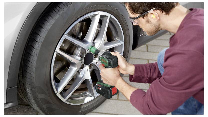 Eine Person verwendet eine Bohrmaschine, um die Metalllegierungsfelge eines Autorads zu reinigen und sich dabei auf einen einzelnen Speichen zu konzentrieren. Das Bild zeigt Wartungsarbeiten am Auto.