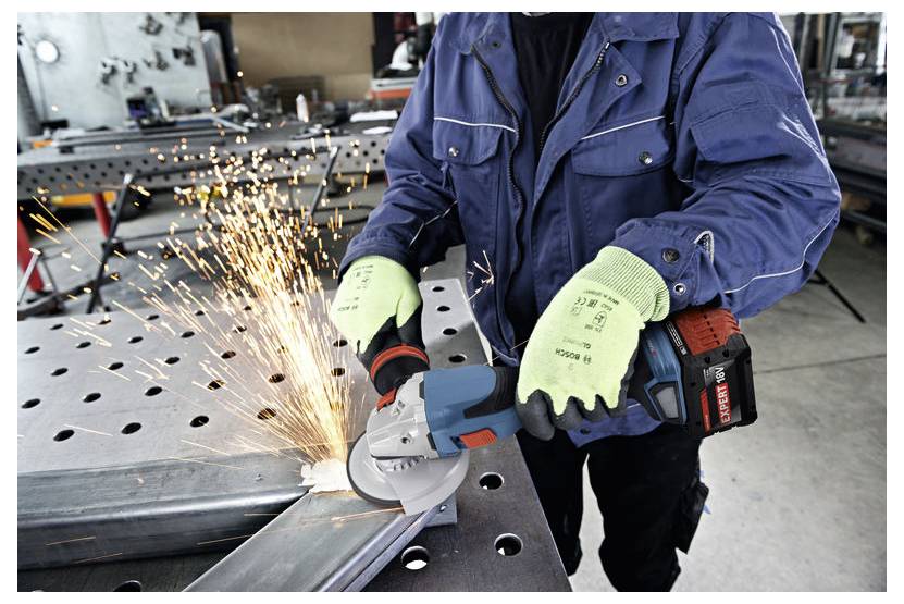 Eine Person mit Sicherheitsausrüstung verwendet ein Elektrowerkzeug, um Metall auf einer Werkbank in einer industriellen Umgebung zu schneiden, wobei Funken entstehen.