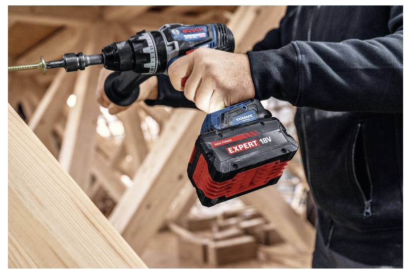 Eine Person verwendet einen 18V-Bosch-Akkuschrauber, um eine Schraube in ein Holzbrett zu schrauben, vor dem Hintergrund einer Baustelle.