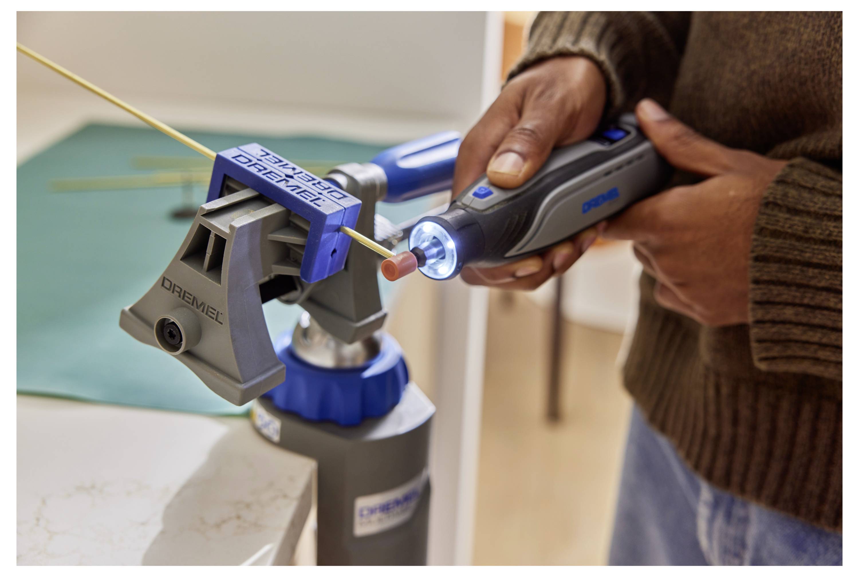 Eine Person benutzt ein Dremel-Werkzeug mit einem Schleifaufsatz, um eine in einem kleinen Schraubstock befestigte dünne Stange zu formen und damit eine DIY-Aktivität zu demonstrieren.