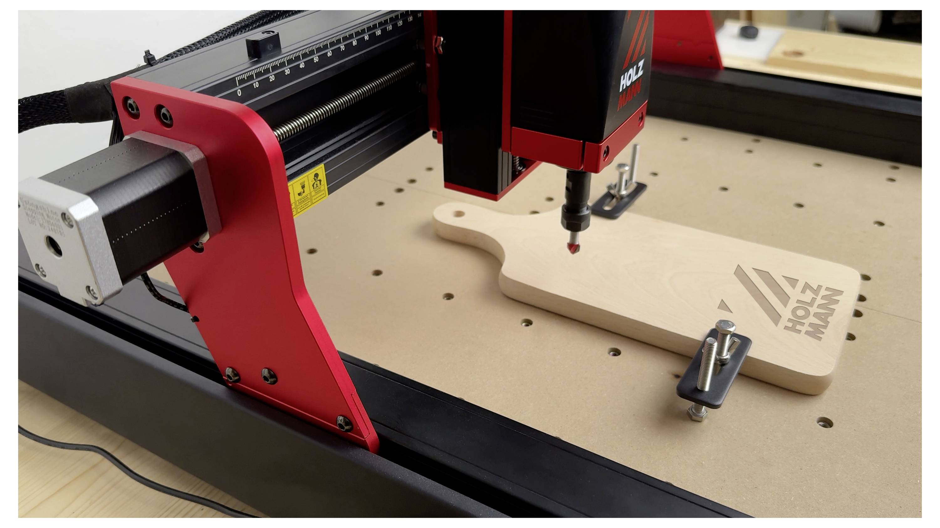 Eine Lasergravurmaschine ätzt ein Design auf ein Holzschneidebrett, das auf dem Arbeitstisch befestigt ist.